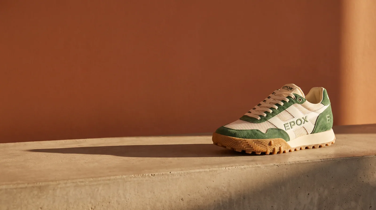 Suede runner sneaker on a long plinth, wide ad with open wall for a headline