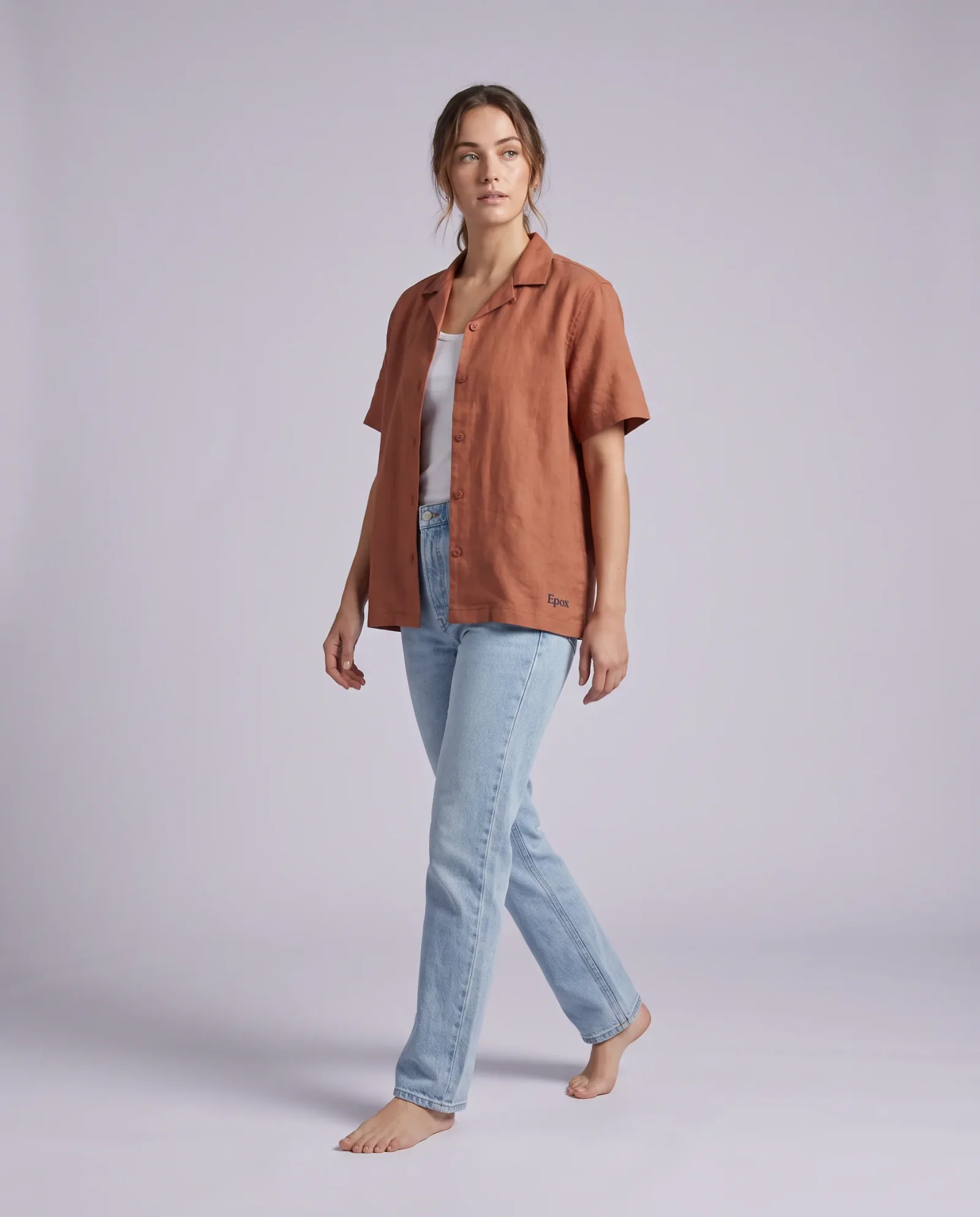 Model wearing a rust linen camp shirt on a pale studio backdrop