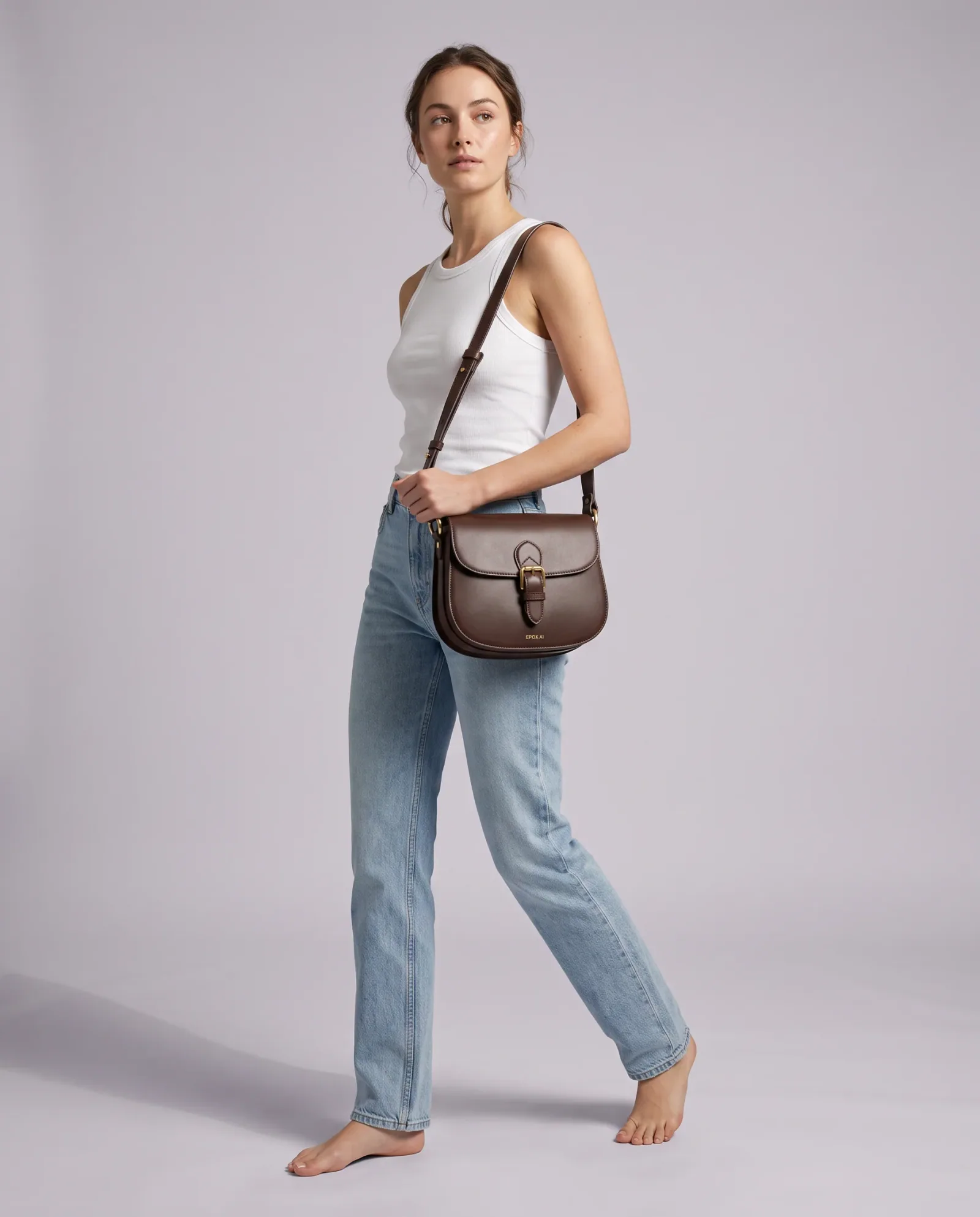 Model carrying a brown leather saddle bag on a pale studio backdrop