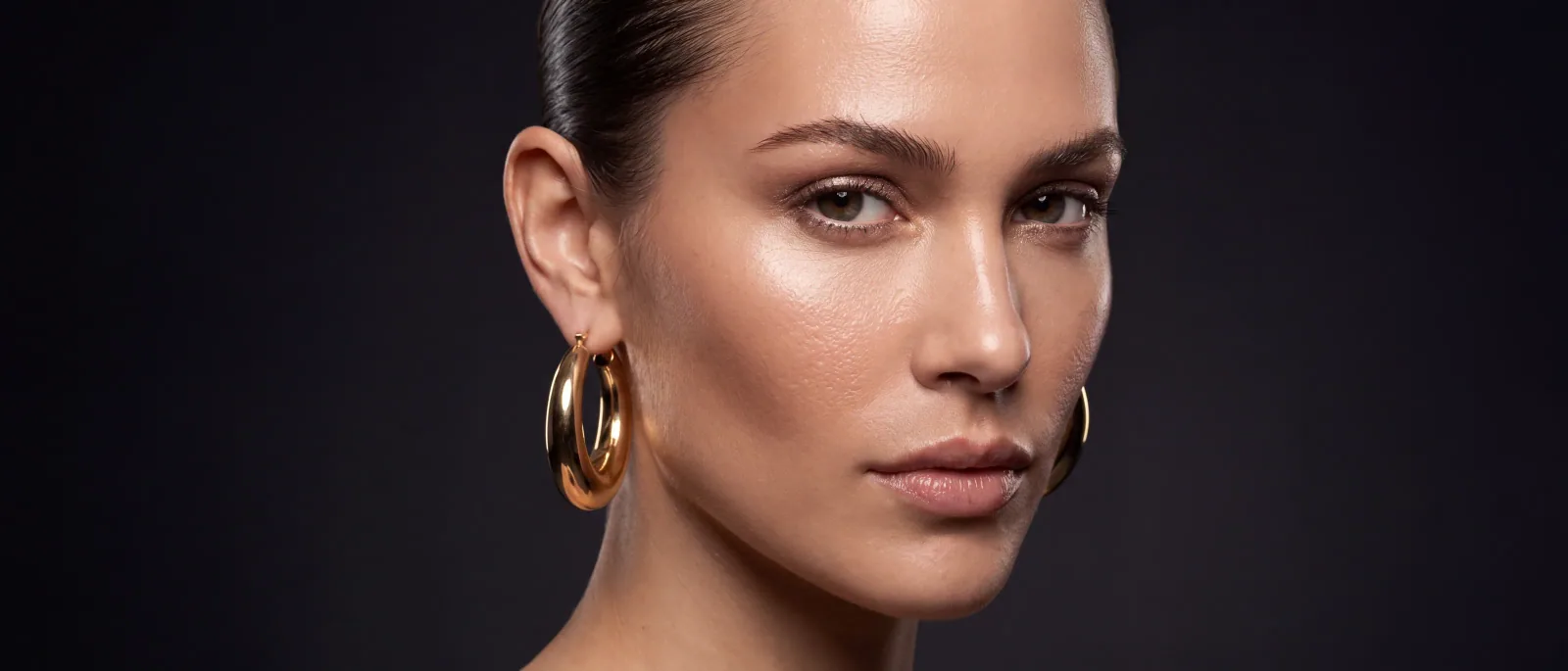 A model wearing a gold hoop earring against a dark ground — Epox on-model still