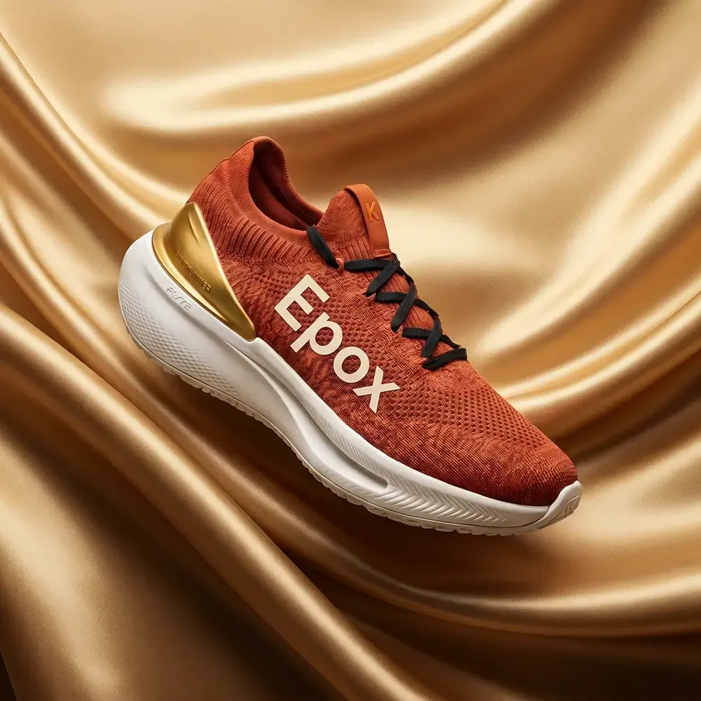 Rust knit running shoe on gold satin — styled packshot