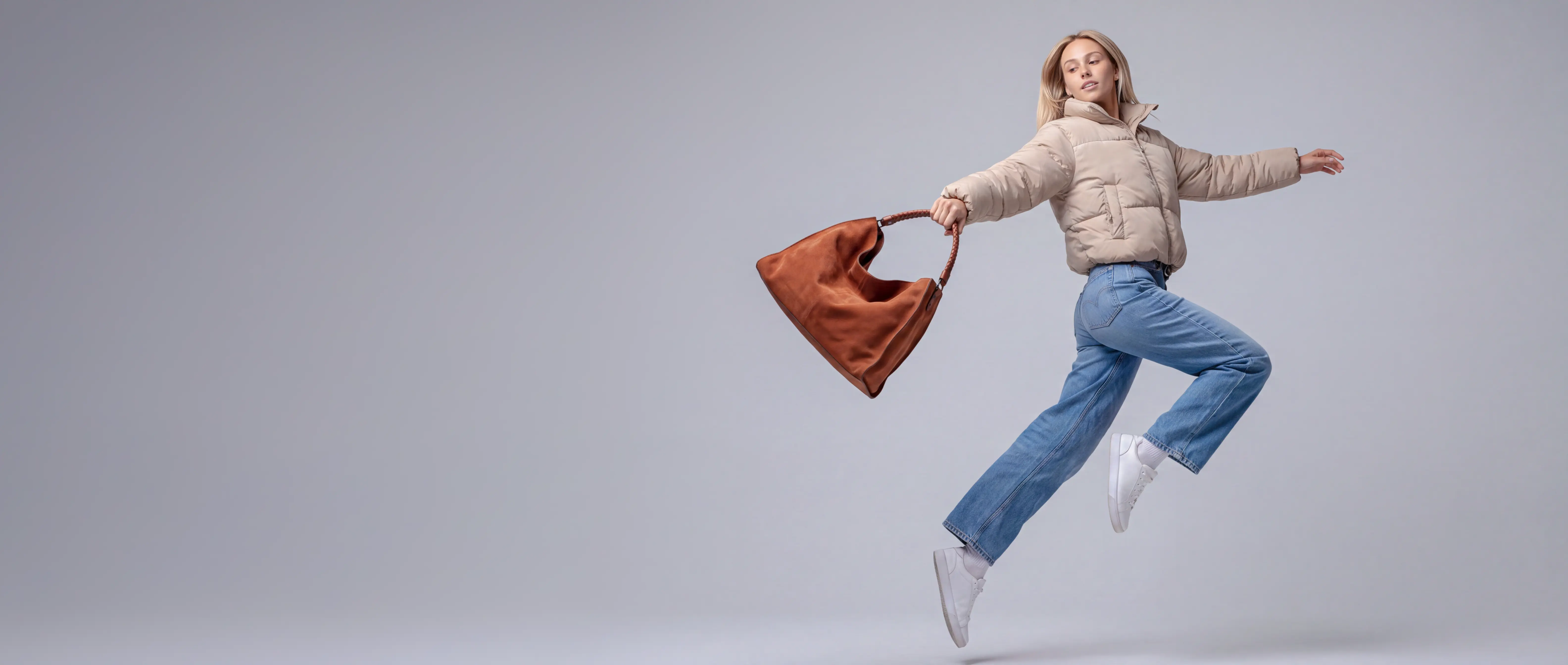 A model mid-leap in a cream puffer jacket and jeans, carrying a suede tote — Epox campaign still